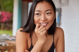 A young asian woman smiling with her hand on her chin at a Wellness Services facility.