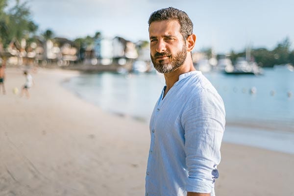 a man in a blue shirt standing on a tropical beach