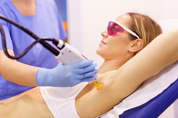 a woman in colored glasses receiving laser hair removal treatment to her underarms