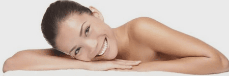 A woman enjoying wellness services in a Cincinnati laser center, lying on a white towel with a smile on her face.